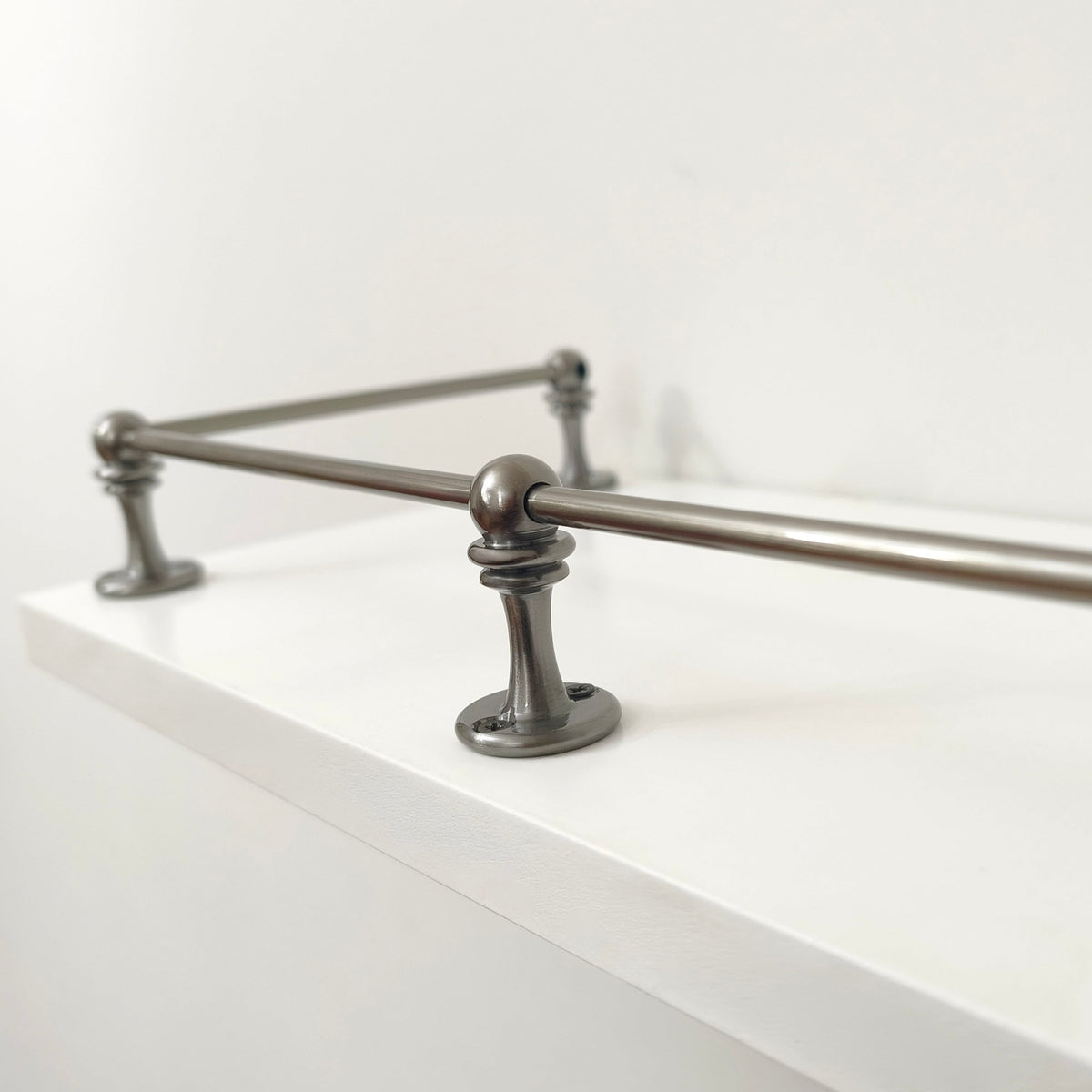 Close-up view of a Black Shadow solid brass corner post and rod assembly mounted on the edge of a white shelf.