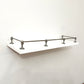 Full front angle view of a Black Shadow solid brass gallery rail system installed around three sides of a white floating shelf.