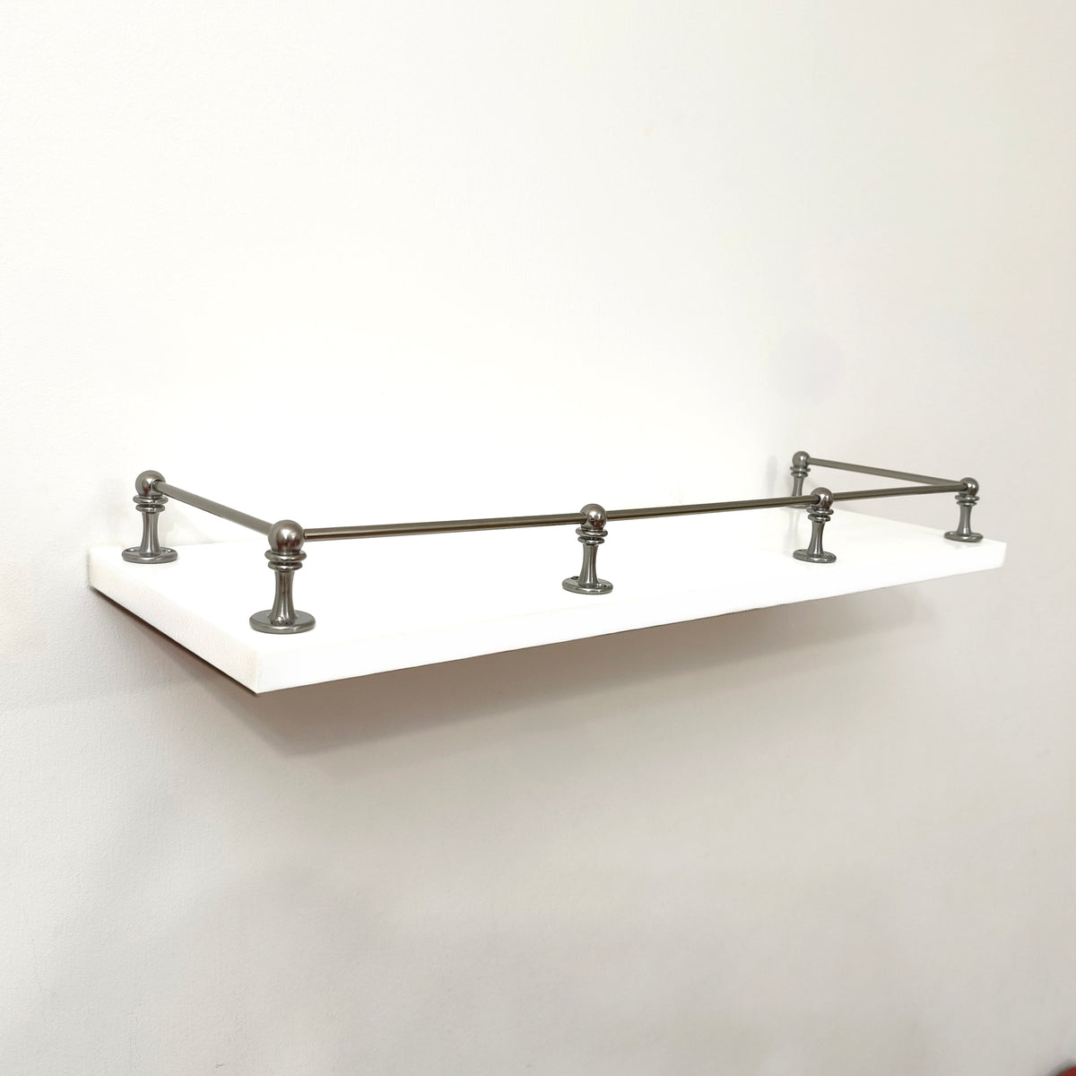 Full front angle view of a Black Shadow solid brass gallery rail system installed around three sides of a white floating shelf.