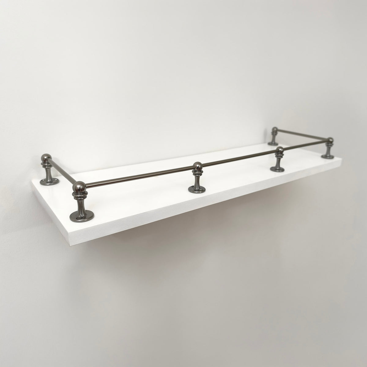A clean, three-quarter perspective view of the fully installed Black Shadow solid brass gallery rail system on a white floating shelf, showing its sleek, dark finish without any text labels.