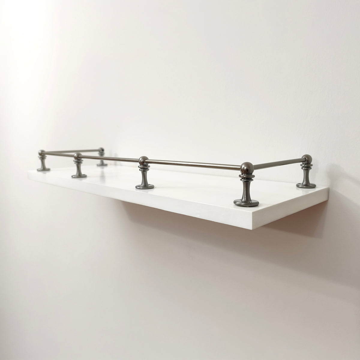 Black Shadow solid brass gallery rail system with corner and middle posts mounted on a floating white wall shelf.