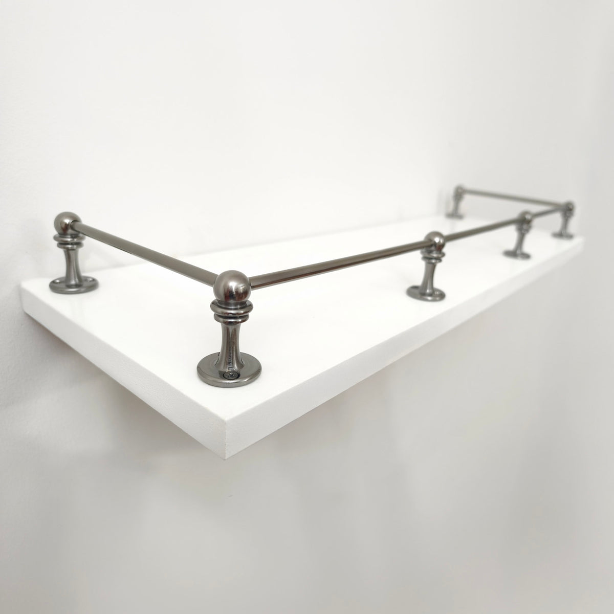 Perspective side view of Black Shadow solid brass gallery rail mounted on a white floating shelf focusing on the front corner post.