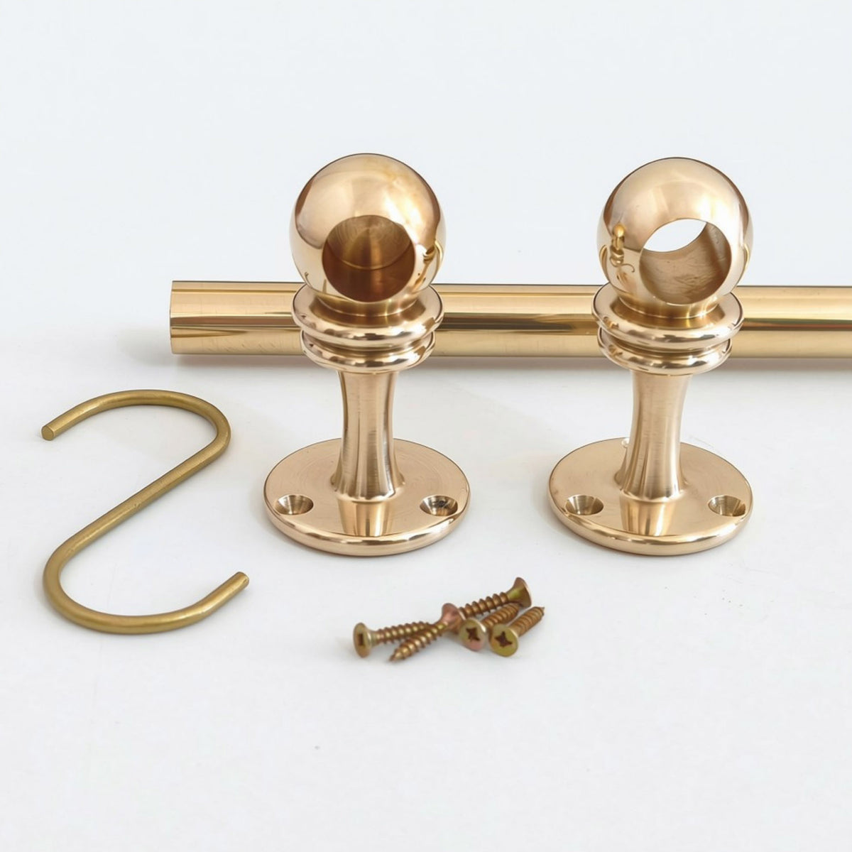 Unlacquered brass kitchen rail hardware kit featuring a solid brass rod, two spherical mounting posts, a matching S-hook, and installation screws, all displayed on a white surface.