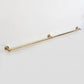 Side angle view of an extra long wall-mounted unlacquered solid brass kitchen rail with center support post on a clean white background.