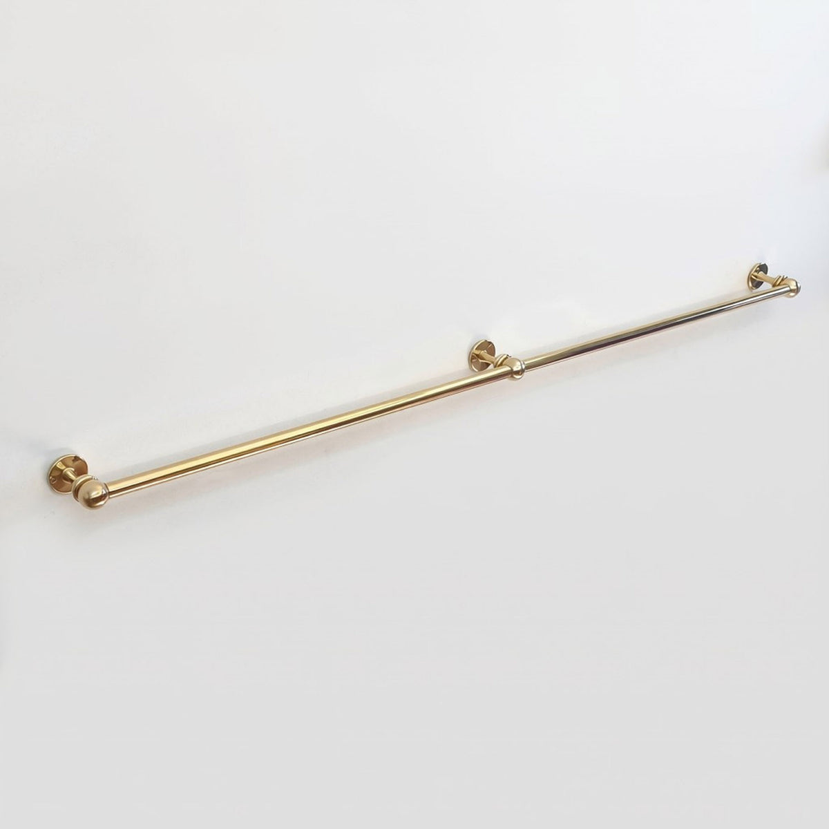 Side angle view of an extra long wall-mounted unlacquered solid brass kitchen rail with center support post on a clean white background.