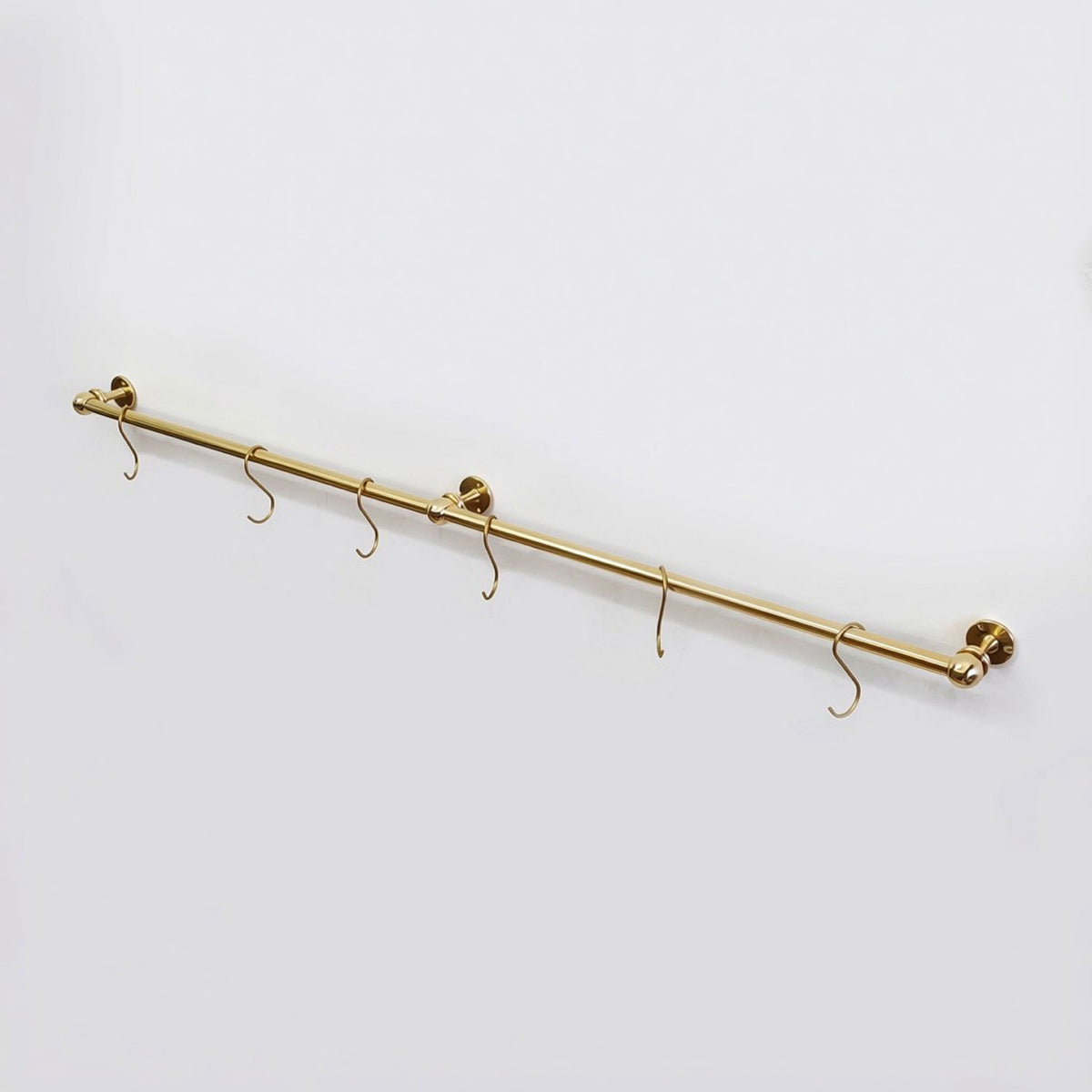 High-angle view of an unlacquered solid brass kitchen hanging rail mounted on a white background with six S-hooks.